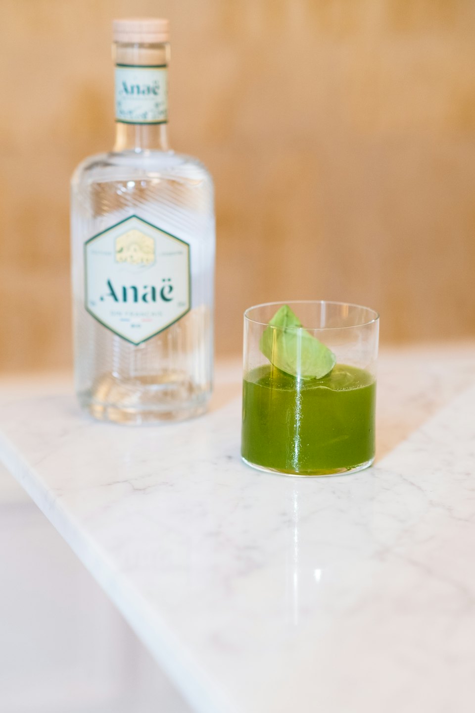 Green cocktail in a glass next to a bottle on a marble counter.